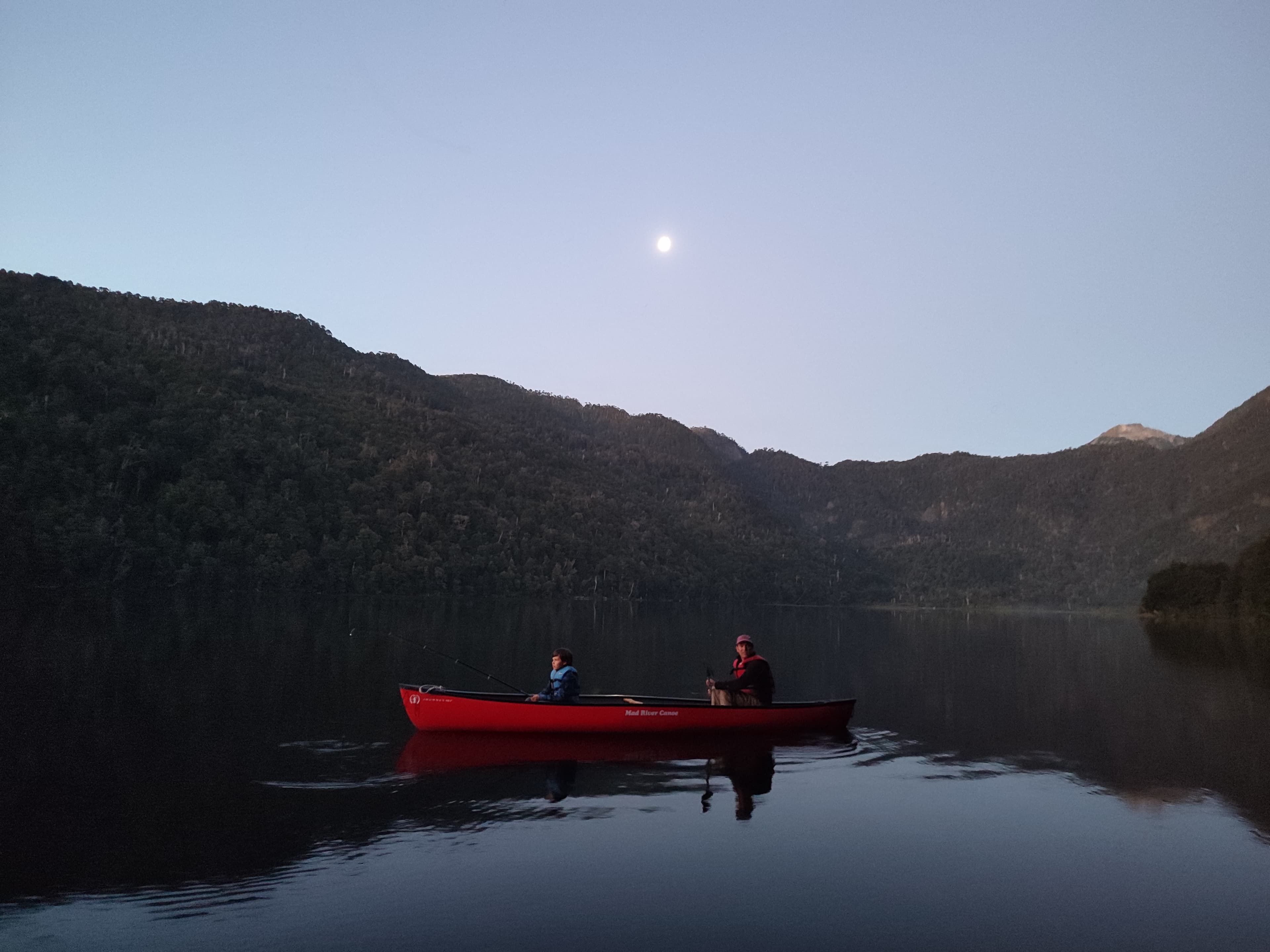 Canoa roja con dos personas en el Lago Tinquilco al atardecer bajo la luna llena