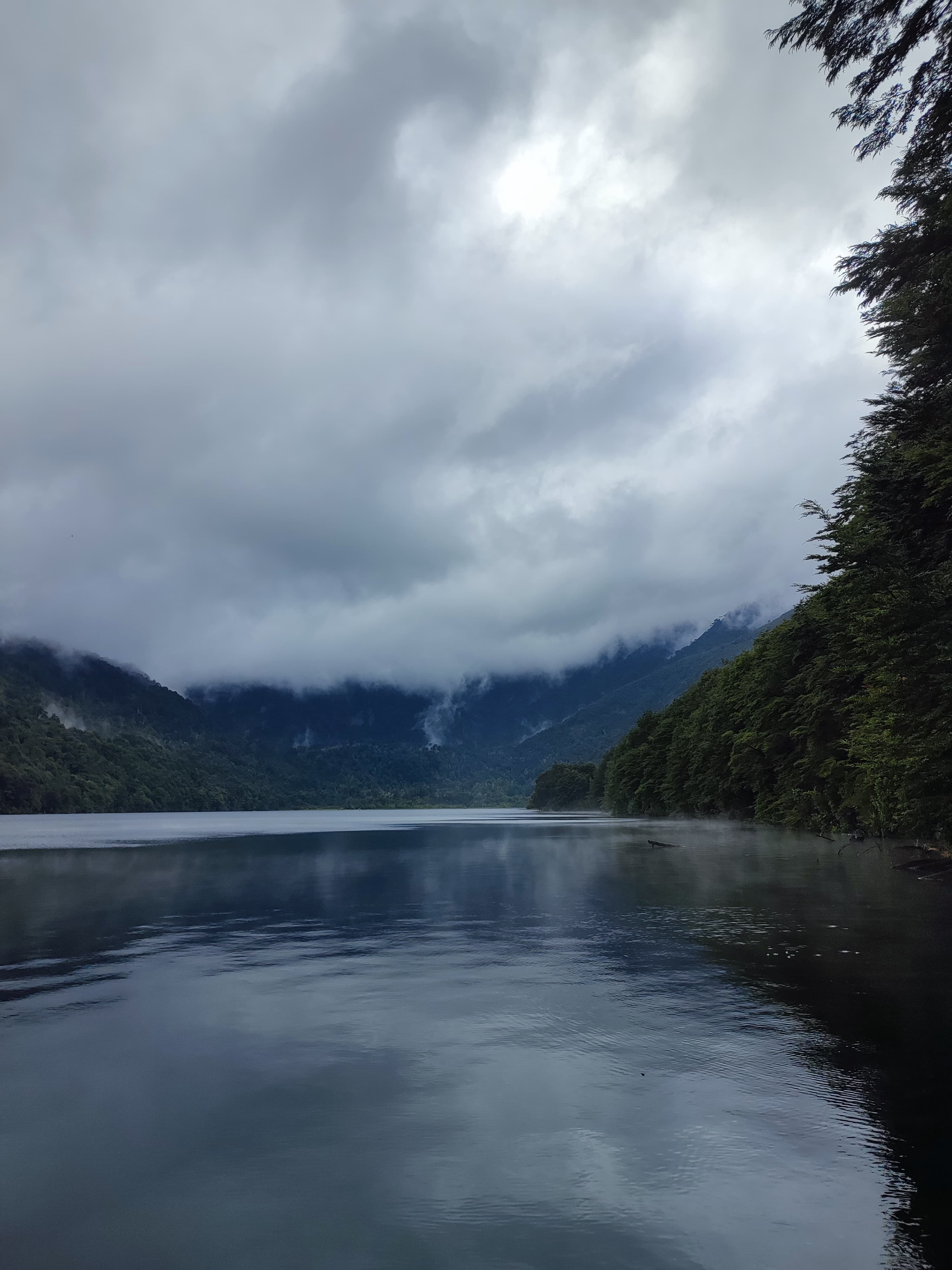 Lago Tinquilco en día nublado con niebla sobre las montañas y bosque de lengas a los lados