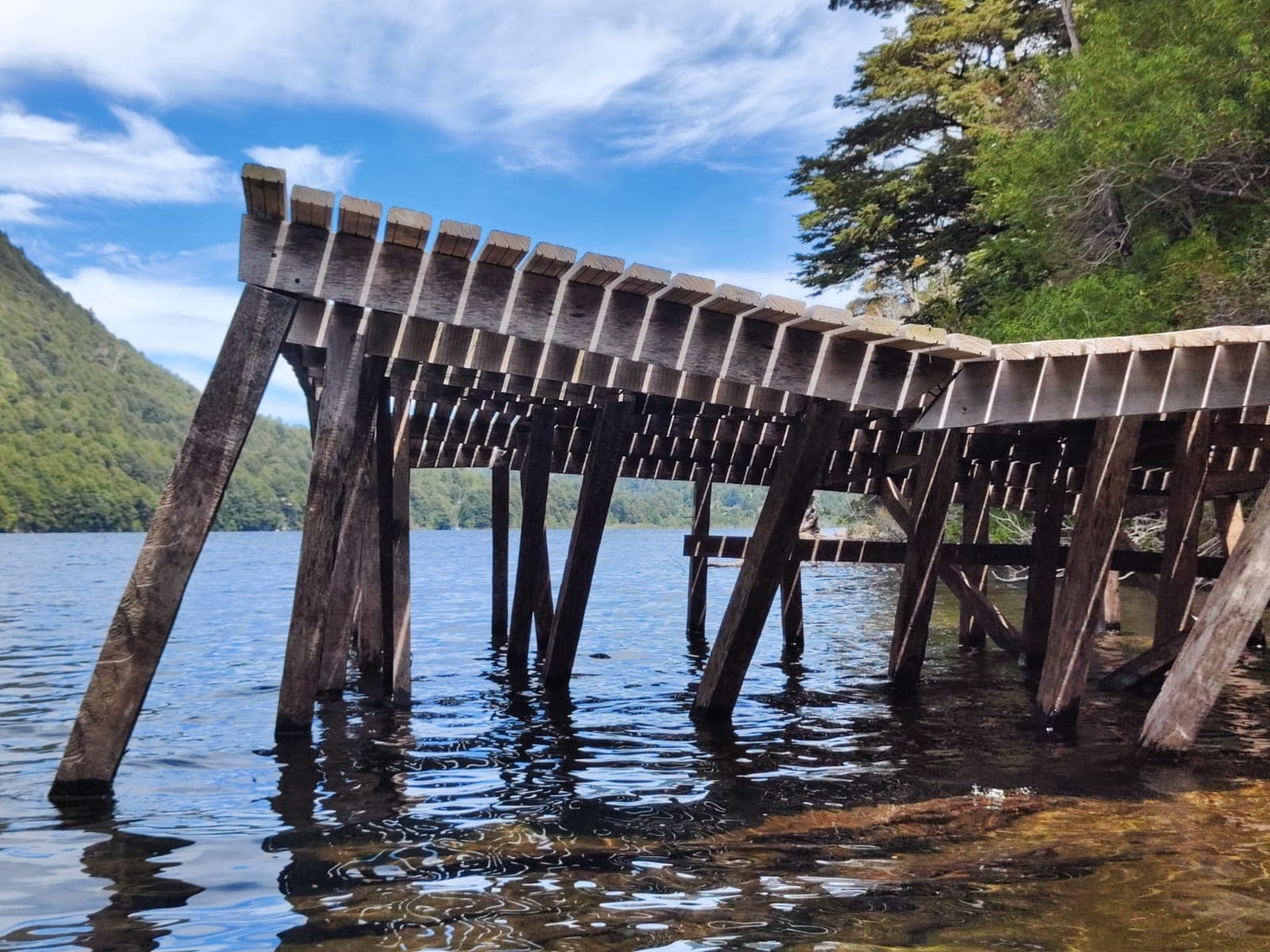 Muelle de madera del Lago Tinquilco visto desde el agua con bosque nativo y cielo azul